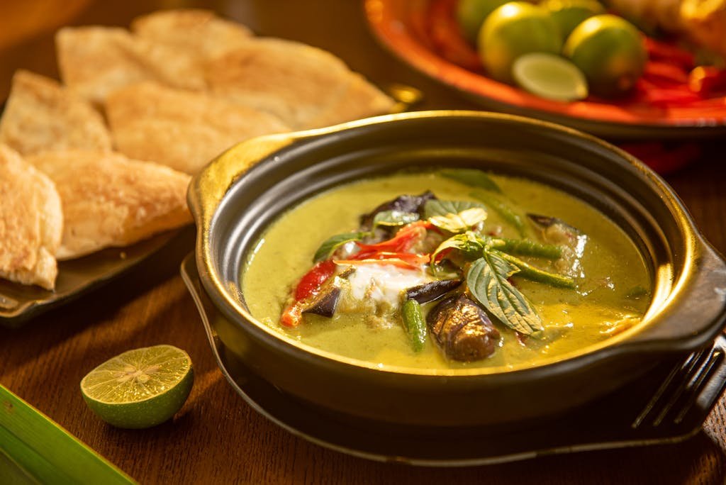 A flavorful vegan Thai green curry with vegetables and aromatic herbs in a stylish black bowl.