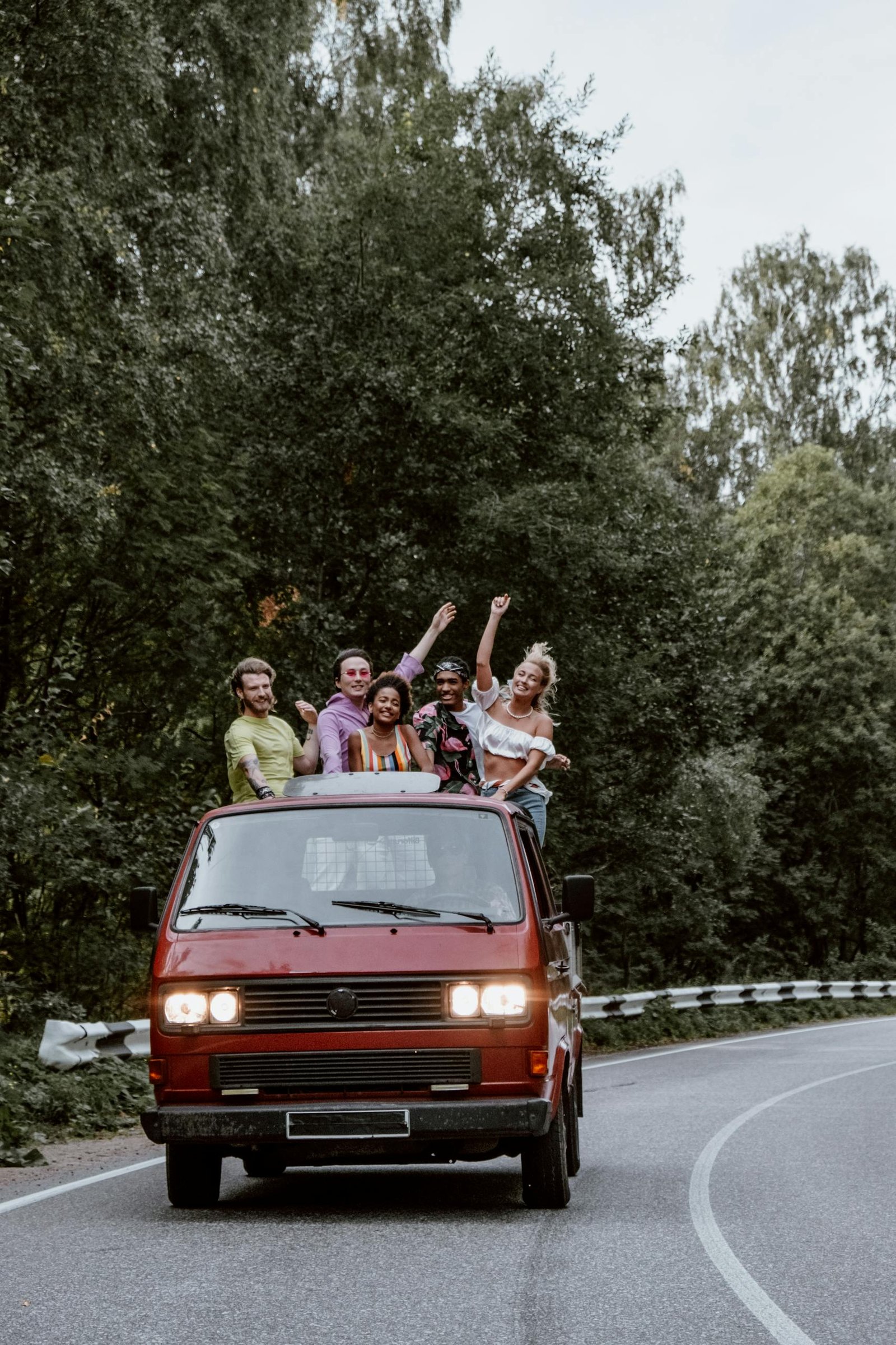A diverse group of friends having fun on a road trip in a vintage van through a scenic forest.