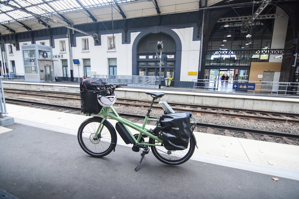 A green cargo bike parked at a railway station platform in France, highlighting sustainable travel.