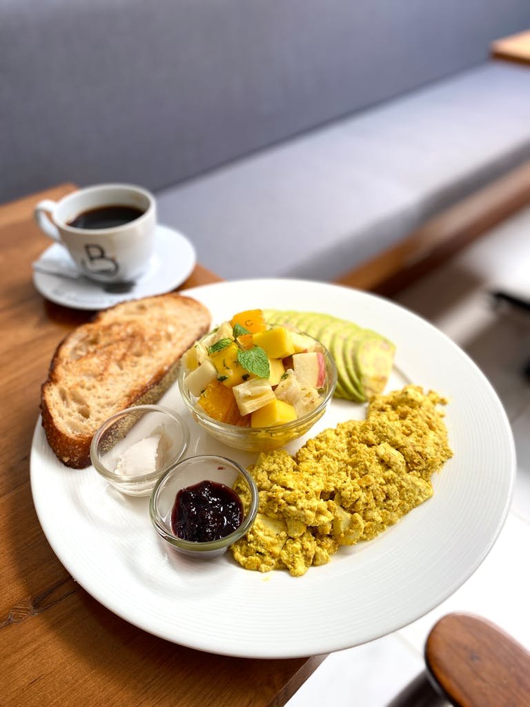 Fresh and colorful vegan friendly hotels breakfast with tofu scramble, fruit bowl, avocado, and coffee.