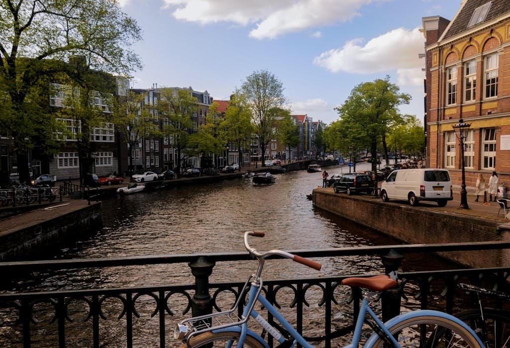 Picturesque view of Amsterdam canal with a bicycle, boats, and classic architecture on a sunny day.