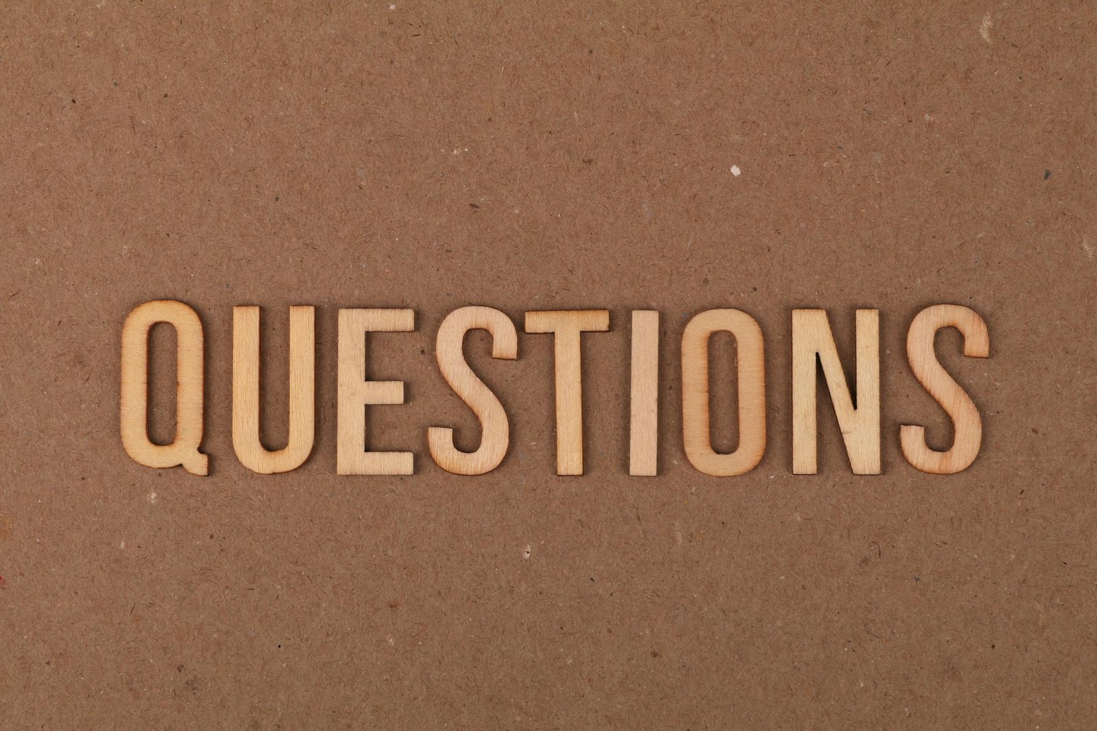 Wooden letters spelling the word "QUESTIONS" on a cardboard background, providing a neutral copyspace.