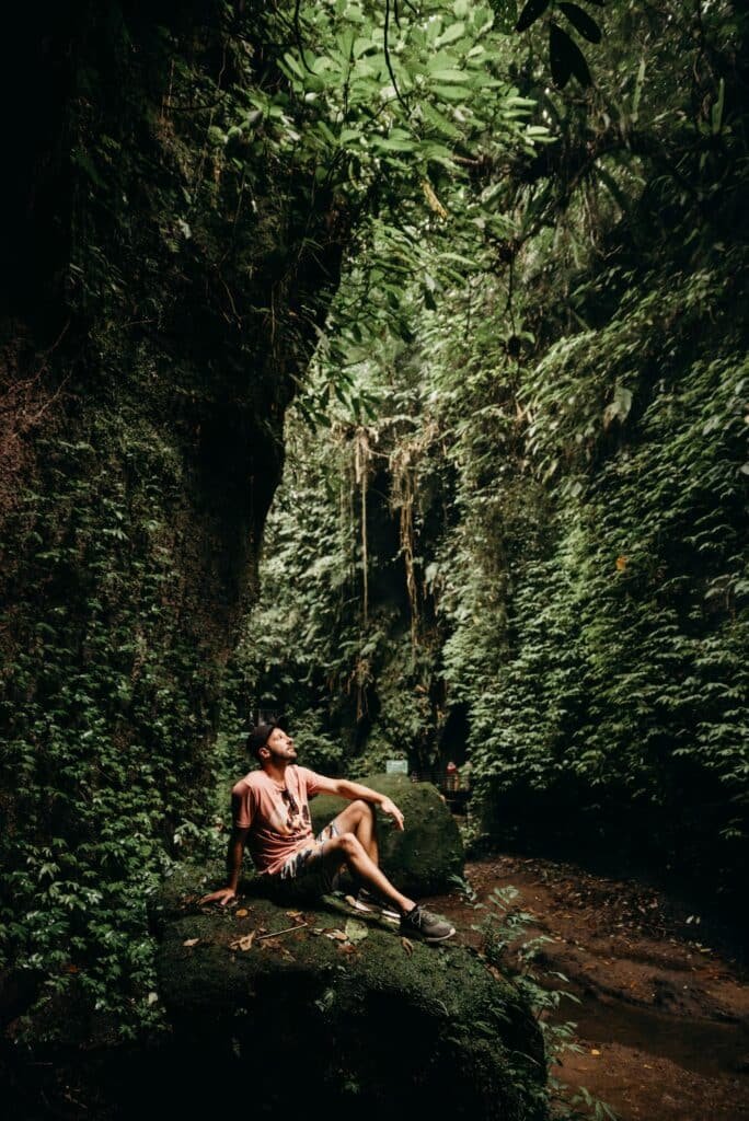 A man sits amidst the lush greenery and rocks of a tropical forest in Bali, Indonesia.