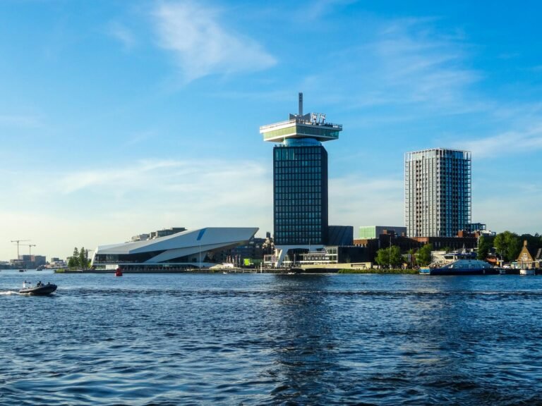 Explore the modern architecture of Amsterdam's skyline along the river with a boat in the foreground.