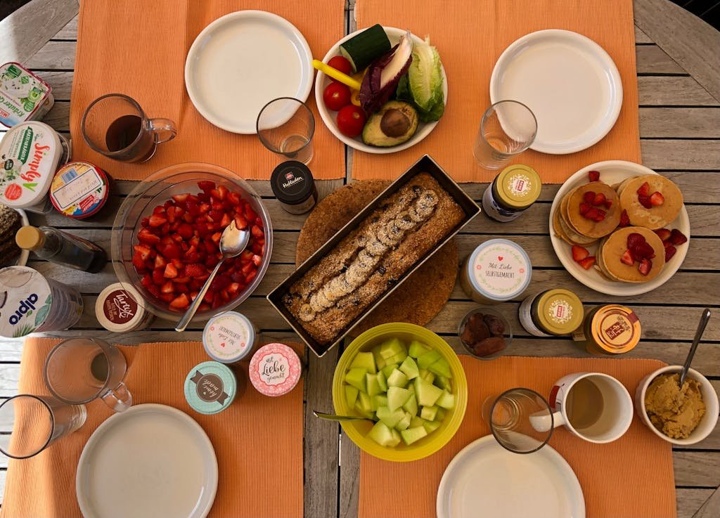 Overhead view of a breakfast spread with fruits, pancakes, and bread on a wooden table.