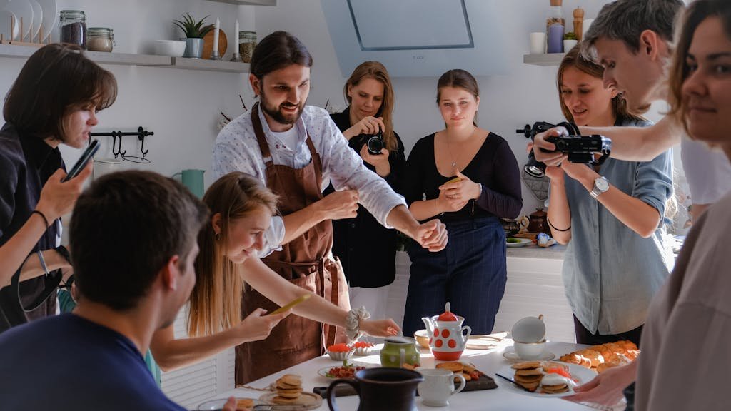 People participating in a lively photoshoot around a table in a bright kitchen.