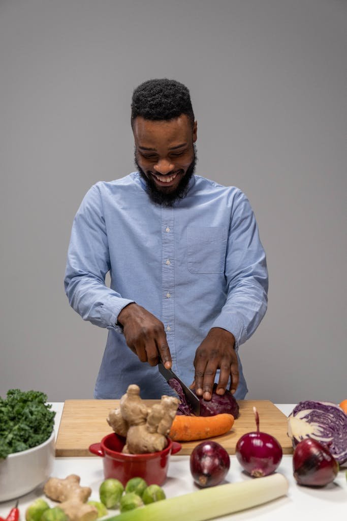 Smiling man slicing red cabbage and vegetables on a wooden board in a studio setting.