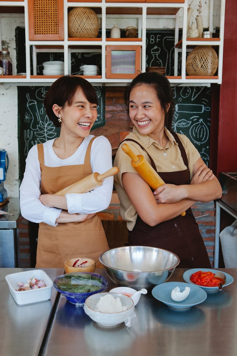 Two women smiling while preparing ingredients in a cozy kitchen setting.