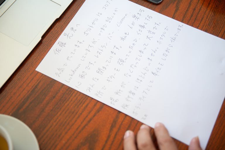 Close-up of a handwritten Japanese letter on a wooden desk with a laptop and tea cup.