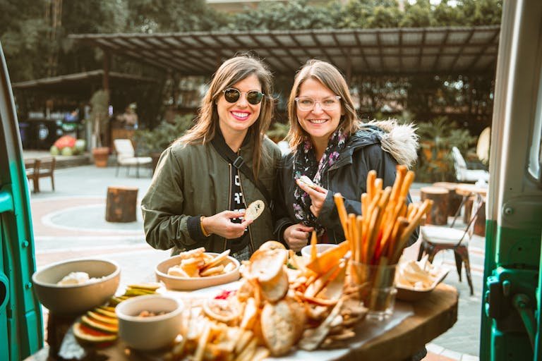 Two women enjoying snacks outdoors, smiling and holding food. Casual and joyful ambiance.
