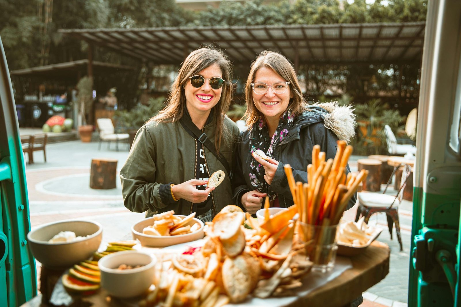Two women enjoying snacks outdoors, smiling and holding food. Casual and joyful ambiance.