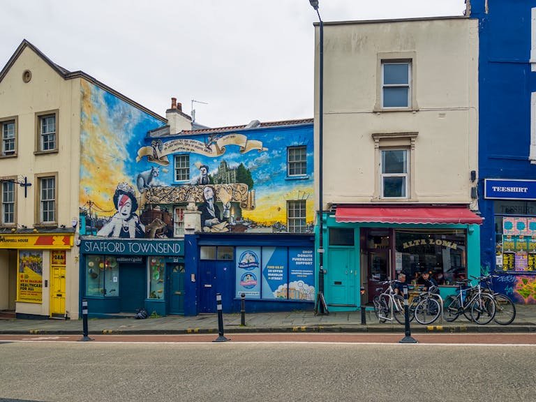 Vibrant street art on houses in Bristol with bikes and shops, showcasing urban culture and creativity.