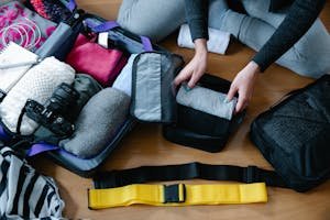 A woman arranging clothes and accessories into a suitcase, preparing for travel.