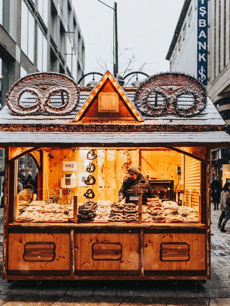 Charming winter scene of a pretzel stand selling goods in a snowy city street at dusk.