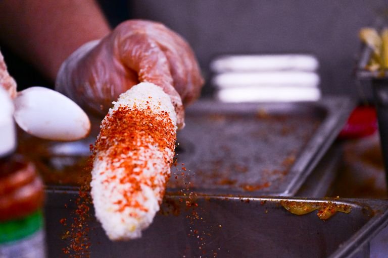 Close-up of a hand preparing Mexican street corn with chili and cheese. Perfect for food lovers.