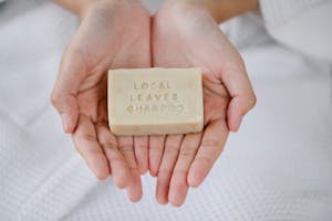 From above of crop anonymous female with simple beige soap in hands on blurred background