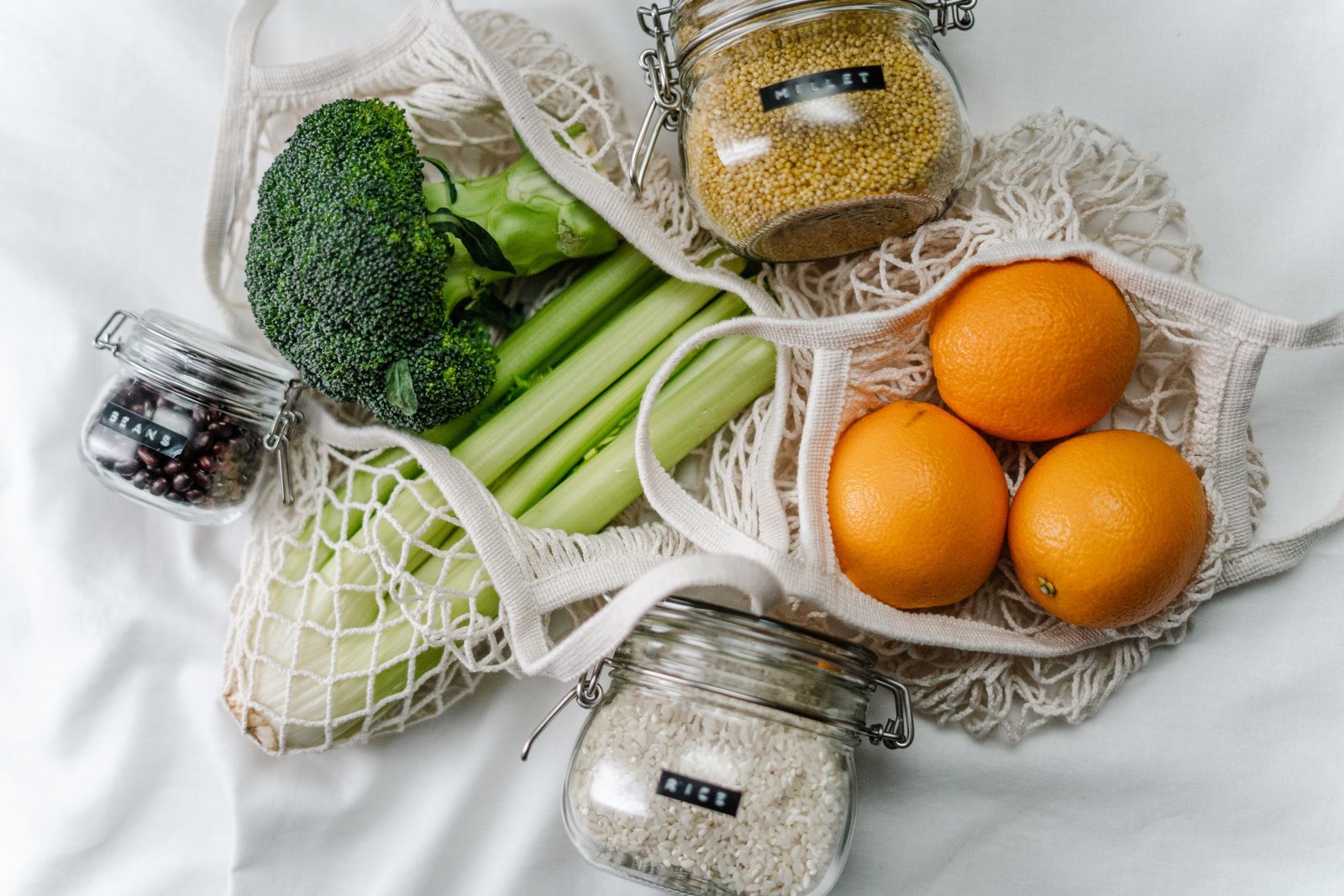 Overhead view of eco bags with broccoli, oranges, and grains in jars, promoting a zero-waste lifestyle.