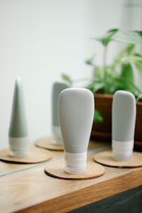 Similar tubes with skincare products placed on coasters on wooden shelf near mirror with green potted plant on blurred background