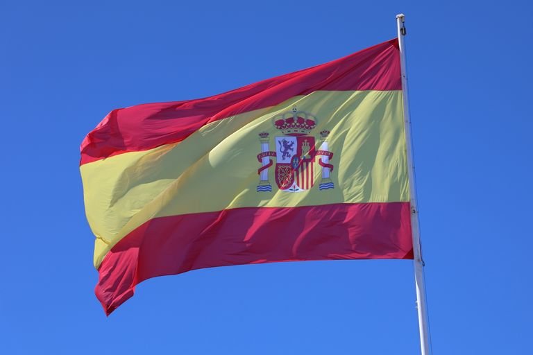 Vibrant Spanish flag waving against a bright blue sky in Cádiz, Spain.