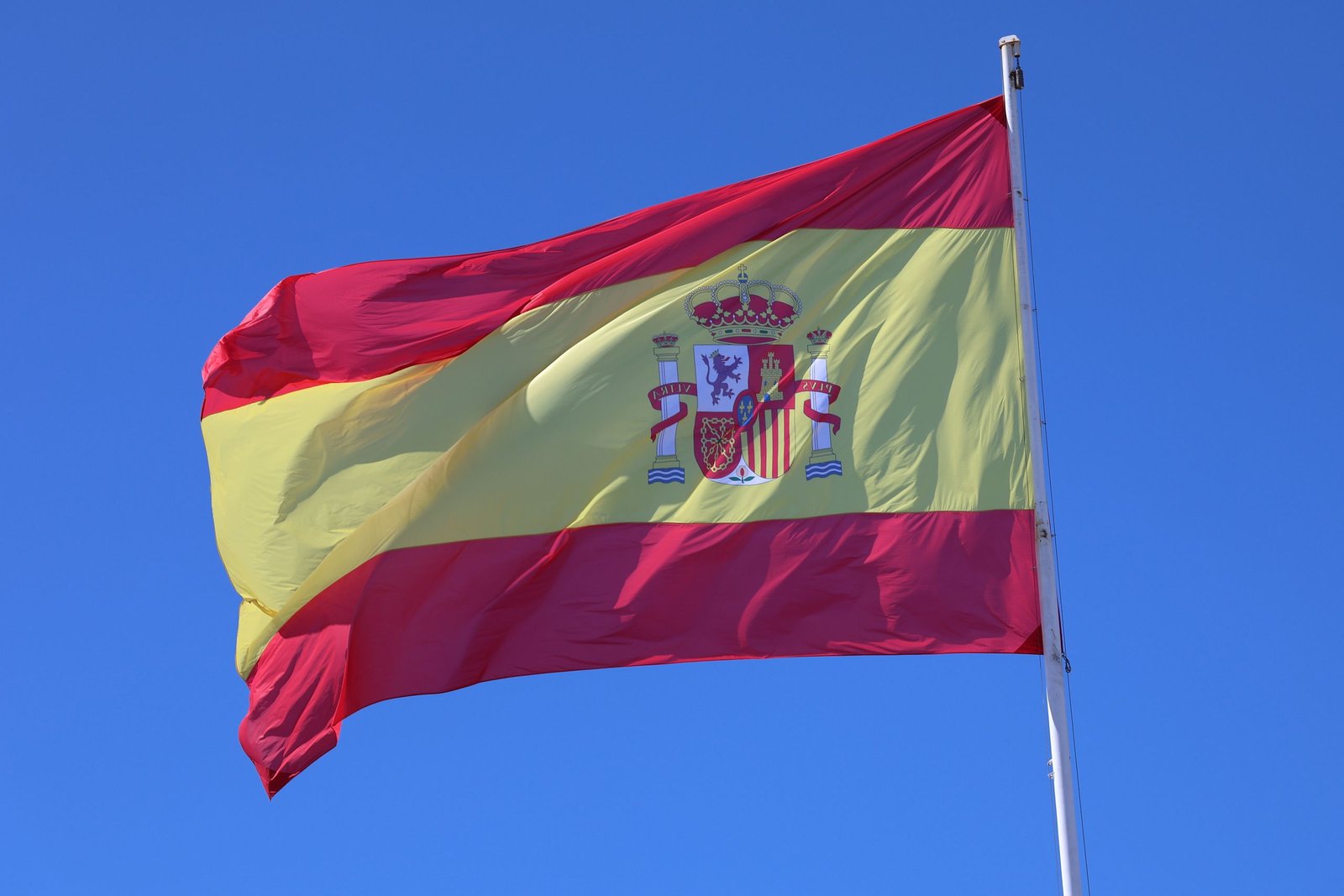 Vibrant Spanish flag waving against a bright blue sky in Cádiz, Spain.