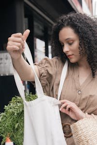 Woman checking eco-friendly tote bag filled with fresh herbs in urban setting.