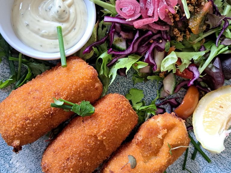 Enjoy crispy fish vegan croquettes paired with a vibrant salad and tangy sauce.