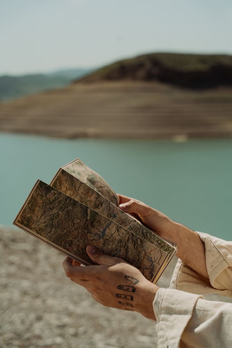 Hands holding a map in a scenic outdoor setting by a tranquil lake.