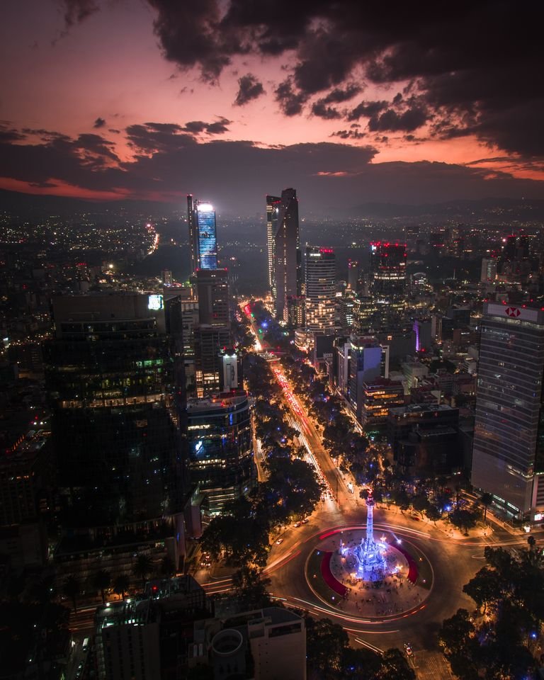 Stunning aerial view of Mexico City skyline during twilight with vibrant city lights and dramatic clouds.
