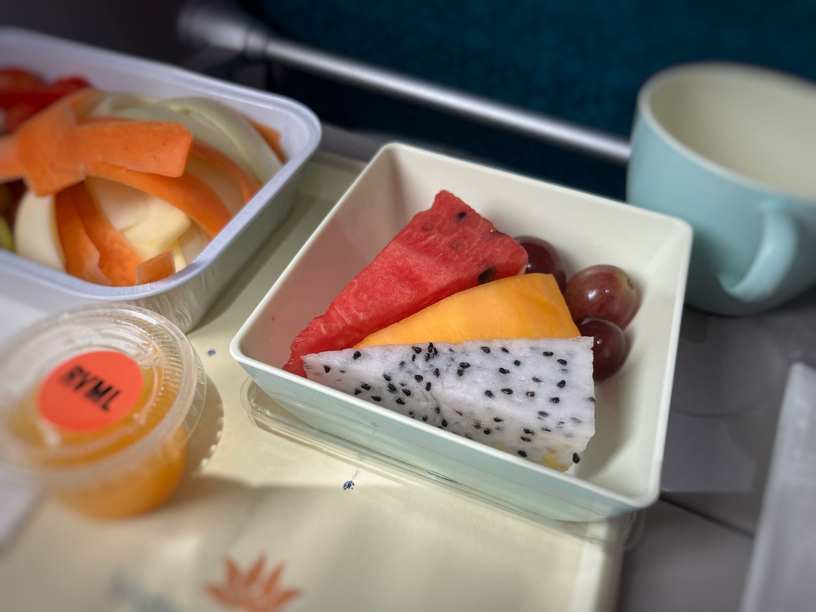 A vibrant airplane meal featuring watermelon, papaya, dragon fruit, and grapes.