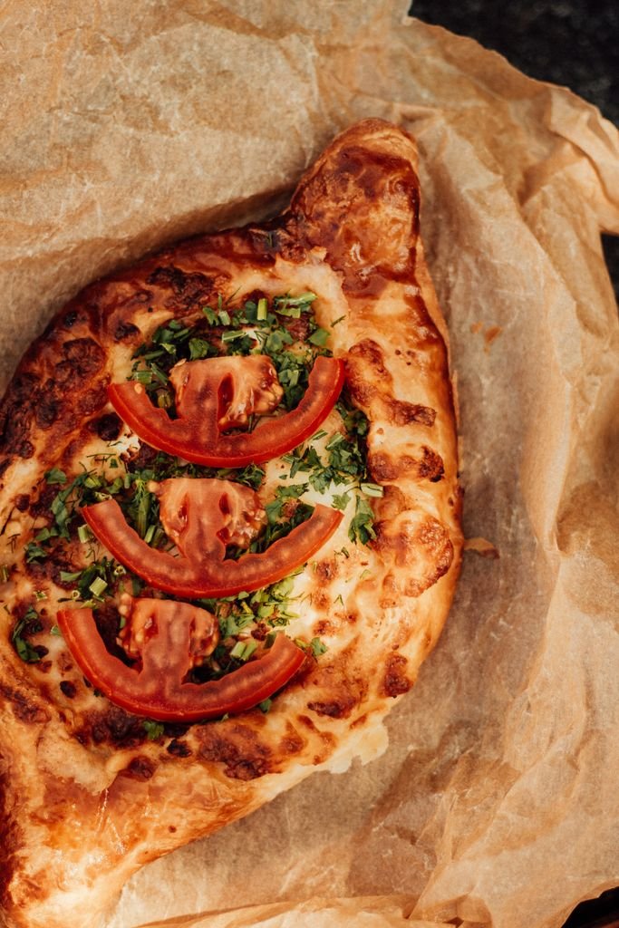 Close-up of baked Georgian Khachapuri with tomatoes and herbs on parchment paper.