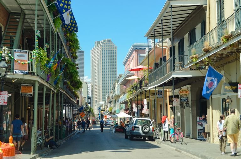 Explore a lively  veganNew Orleans street bustling with pedestrians, cars, and iconic architecture under a clear summer sky.