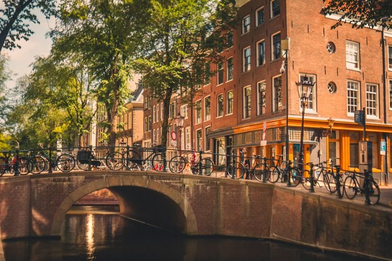 Sunny view of an Amsterdam canal with bicycles on a bridge and historic buildings.